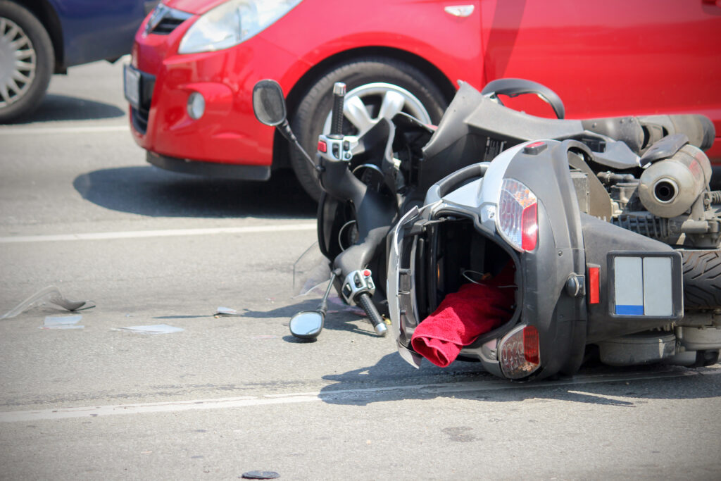 Scooter lying on the road after a traffic accident with a red car in the background.