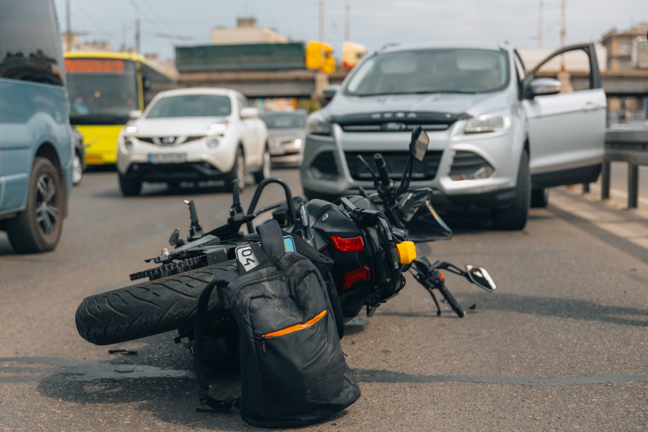 Motorcycle accident on city street involving a car with traffic in the background
