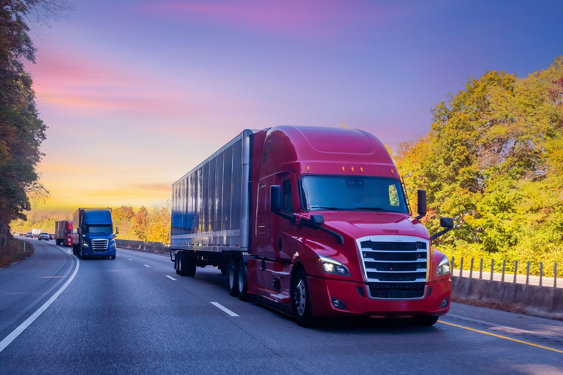 Red semi-truck driving on highway during sunset with other trucks in the distance. Red semi-truck driving on highway during sunset with other trucks in the distance.