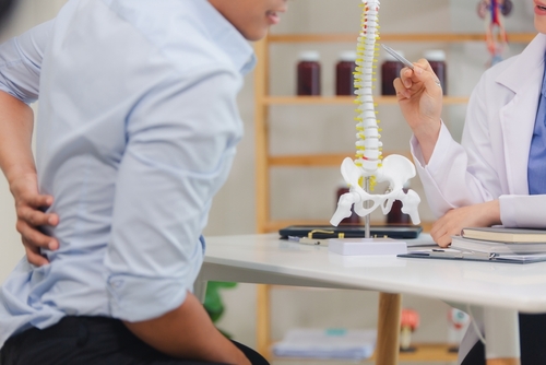 Doctor showing a spine model to a patient during a consultation, illustrating medical evaluation for a spinal cord injury.