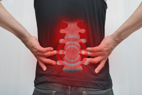 Person holding their lower back with a glowing spine graphic highlighting pain, representing symptoms of a spinal cord injury.